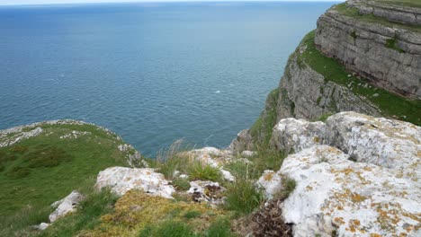 Grasbewachsene-Felsige-Große-Orme-Klippenkante-Mit-Bergblick-Dolly-Mit-Direktem-Blick-Auf-Den-Windigen-Malerischen-Meerblick