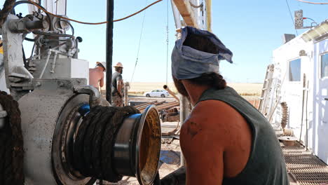 rear view of a man winding the rope on the roller. male workers setting equipment on the site for drilling oil or gas.