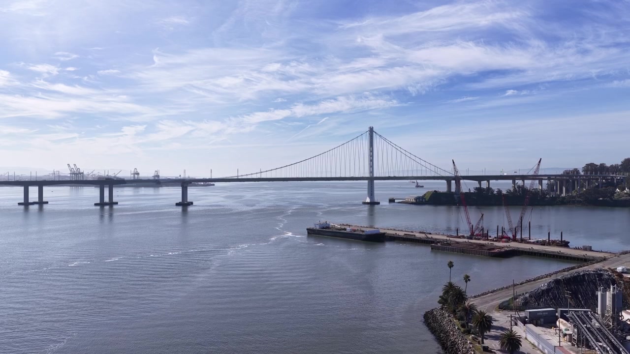 Vista aérea magnífica da Ponte San Francisco-Oakland Bay e da Ilha do Tesouro em uma manhã ensolarada, com uma barcaça navegando nas águas calmas sob um belo céu azul com nuvens esparsas.