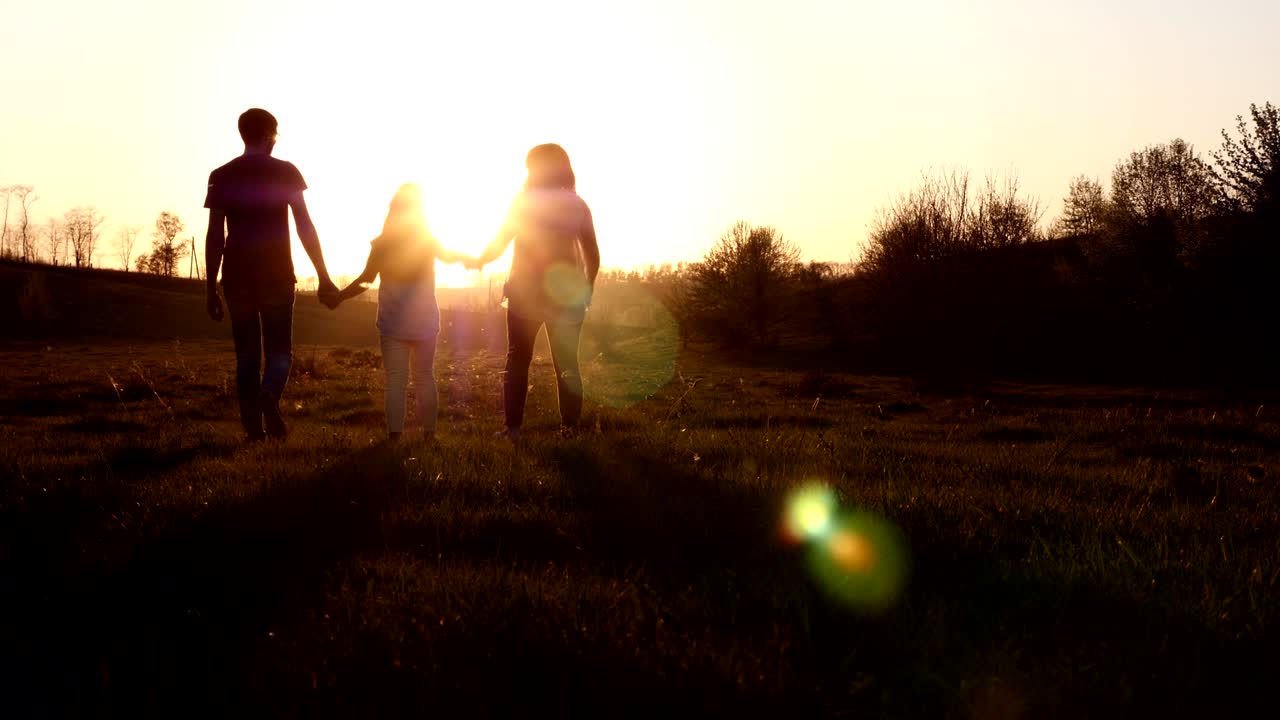 Silhouette of mother and father walking with their daughter at sunset