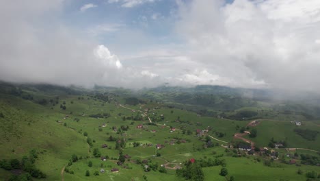 Scattered-villages-among-green-hills-under-a-cloudy-sky,-evoking-a-serene-rural-landscape,-aerial-view