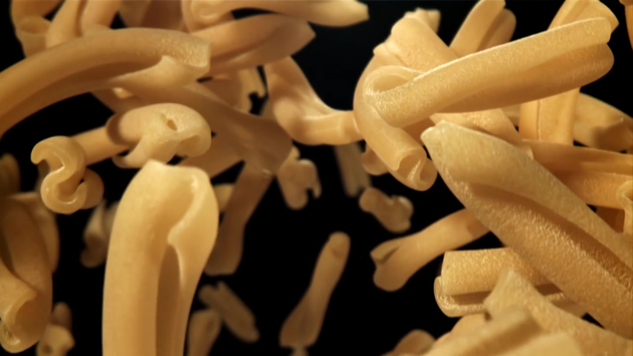 Pasta maccheroni secca che cade al rallentatore su sfondo nero.