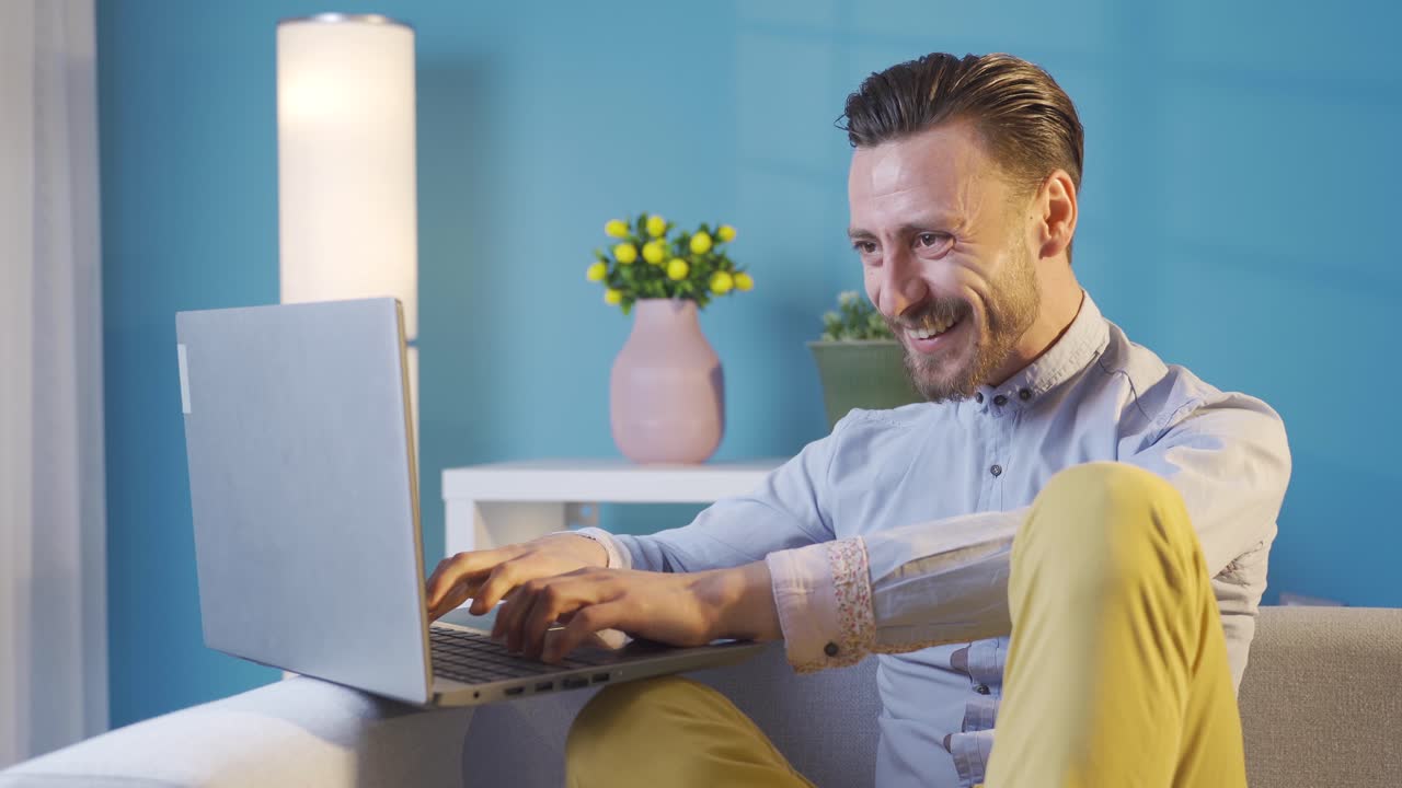 스타일리시하고 카리스마 넘치는 성인 젊은 남자가 집에서 노트북을 사용하여 기 ⁇ 하고, 좋은 소식을 듣고, 승리합니다.