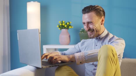 joven adulto elegante y carismático usando una computadora portátil en casa regocijándose, recibiendo buenas noticias, ganando.