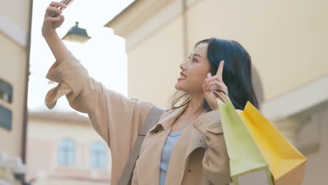mujer asiática feliz joven sonriente chica en ropa elegante de moda con bolsas de compras de colores brillantes está usando su teléfono inteligente mientras camina en el centro comercial