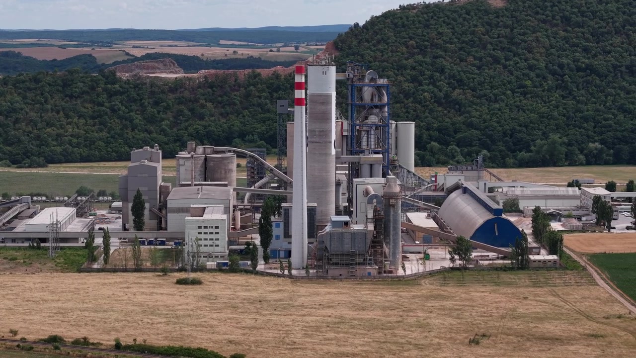 Laaja teollisuuslaitos sijaitsee luonnonmaisemassa, pilvisen taivaan alla
