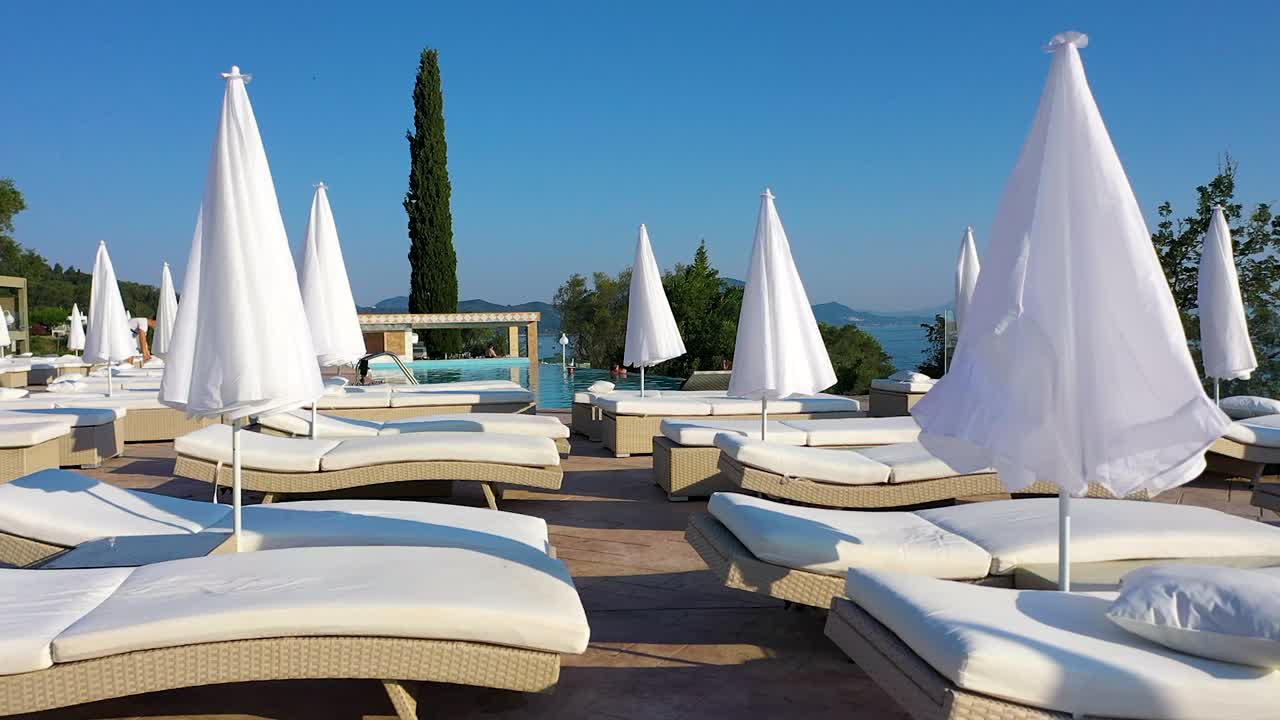 Close up tracking shot of a hotel terrace with pool and sun beds.