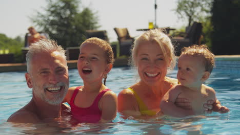 Porträt-Von-Großeltern,-Die-Sich-Mit-Enkelkindern-Im-Sommerurlaub-Der-Familie-Im-Schwimmbad-Vergnügen