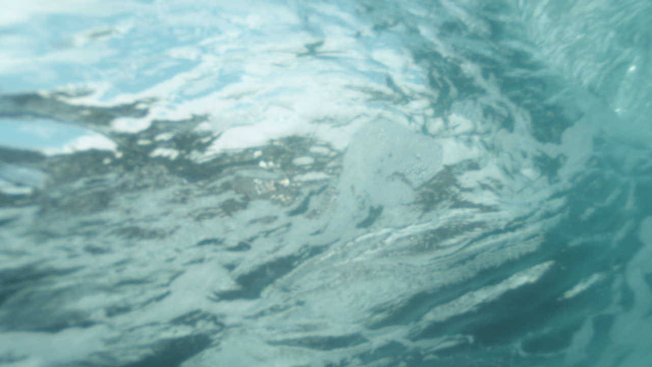Submerged perspective of an ocean wave breaking, with water spray and shifting light visible underwater
