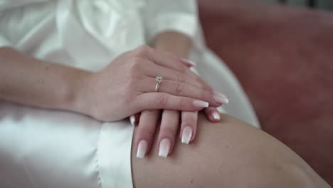 bride's hands resting on her lap, displaying a delicate engagement ring and polished nails