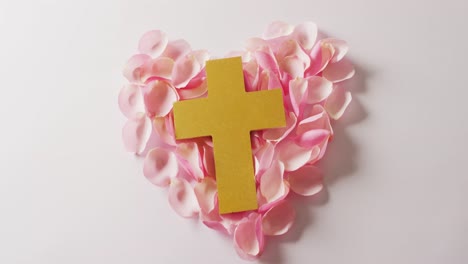 Video-of-yellow-christian-cross-on-heart-shape-of-pink-rose-petals-on-white-background