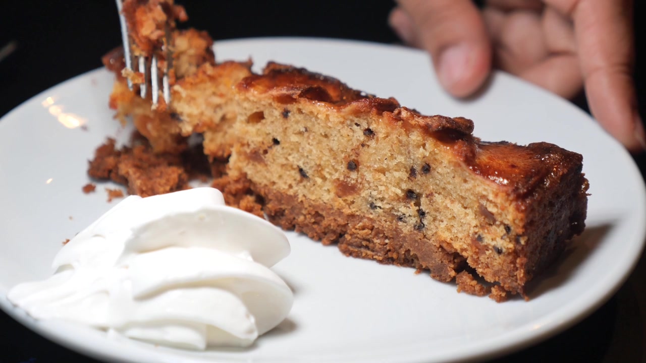 Close-up of a Fork Cutting a Slice of Delicious Cake with Whipped Cream