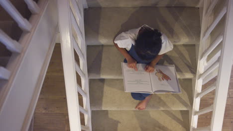 vista aérea de una chica asiática sentada en las escaleras de su casa leyendo un libro