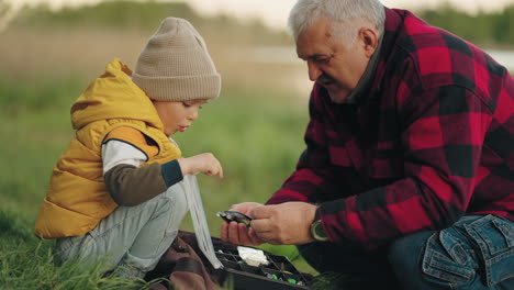 old fisherman is showing to his grandson fishing gear grandfather is teaching little boy