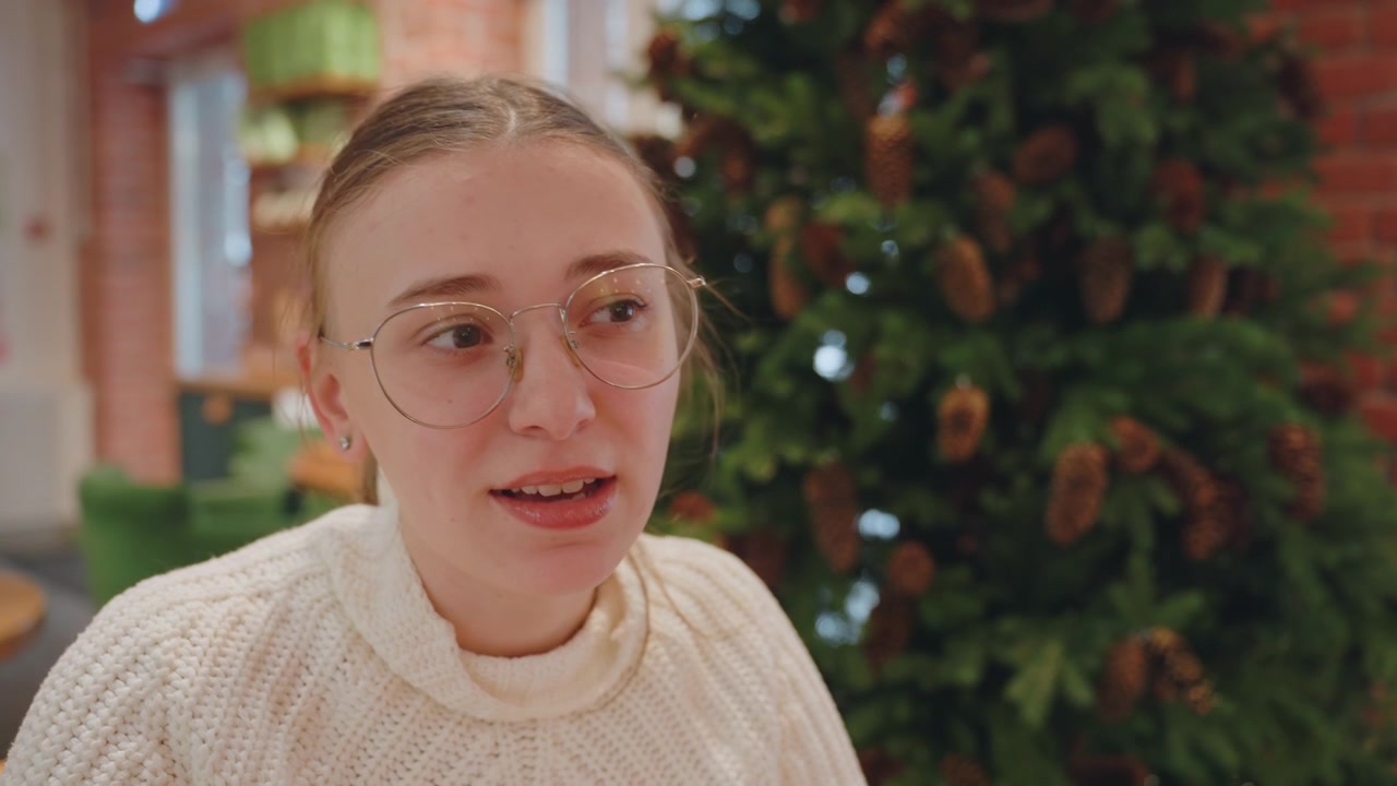 Giovane donna con gli occhiali che conversa accanto all'albero di Natale.