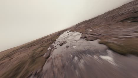 fpv aerial shot of stream and waterfall in an icelandic meadow