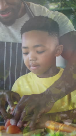 animation of leaves over happy african american father and son cooking together