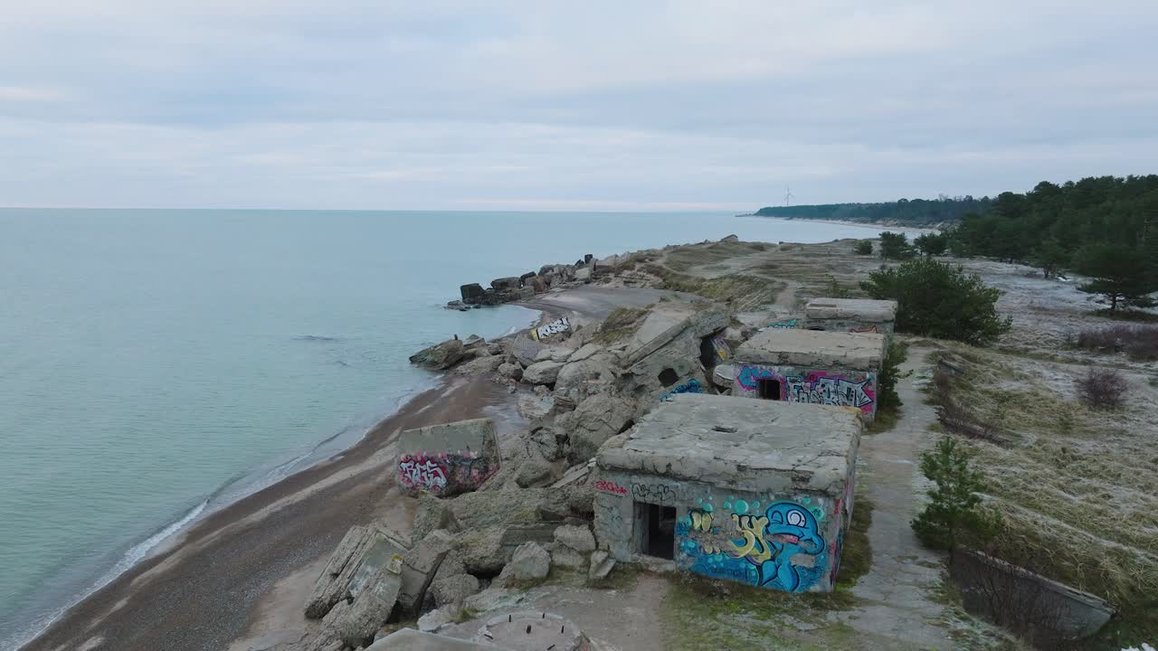 съемка с воздуха заброшенных приморских фортификационных сооружений в северных фортах каросты на берегу балтийского моря, пасмурный день, широкая съемка с дрона, движущаяся вперед
