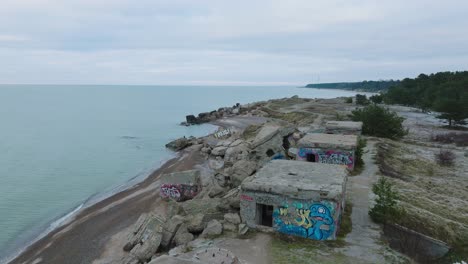 establecimiento de una vista aérea de los edificios de fortificación costeros abandonados en los fuertes del norte de karosta en la playa del mar báltico, día nublado, amplio tiro de drones avanzando