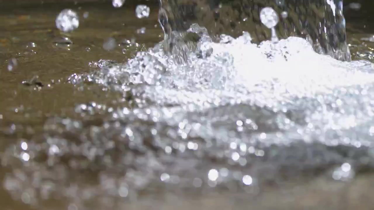 Gros plan fixe d'eau tombant sur une surface en pierre avec un éclairage naturel lumineux.