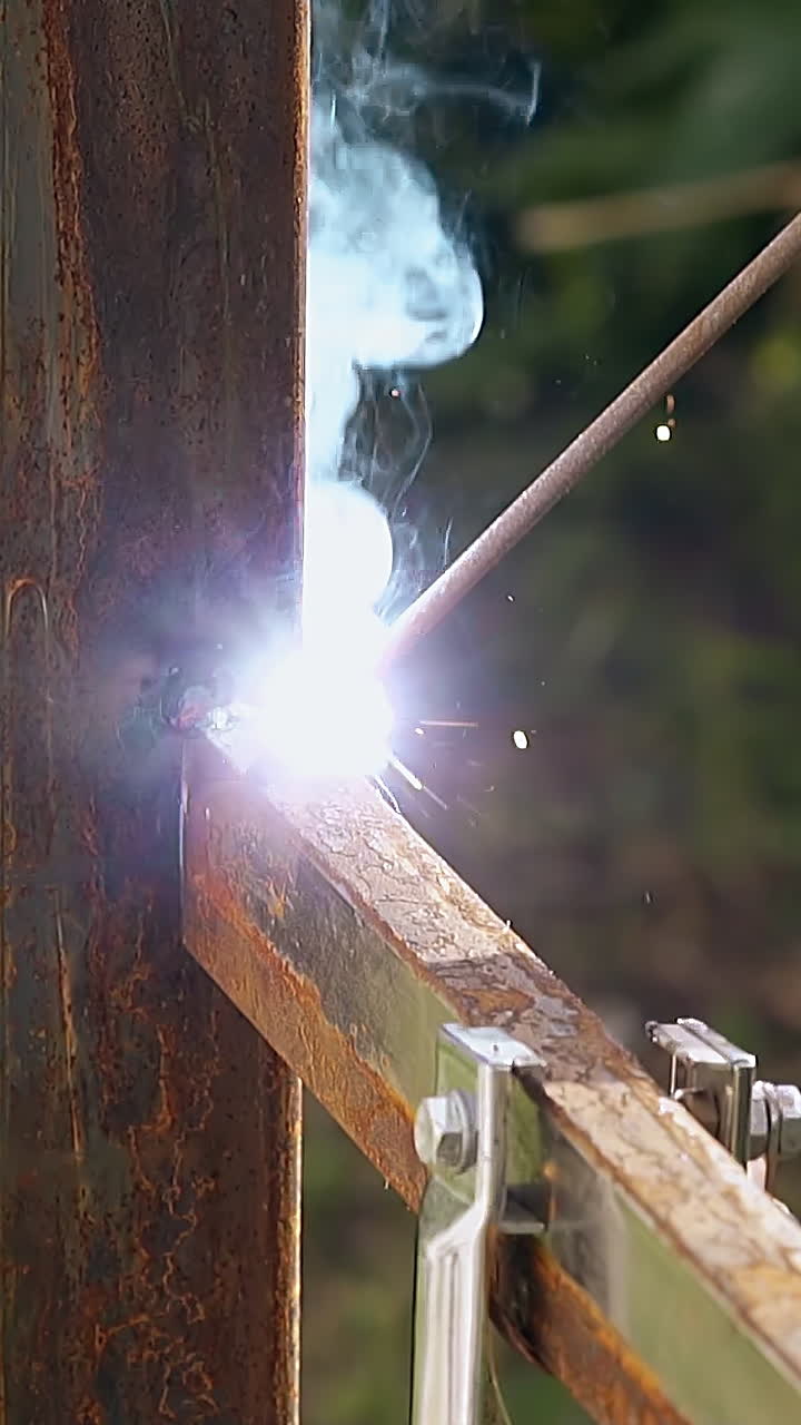 Primo piano del processo di costruzione di una recinzione metallica con l'uso di un attrezzo per saldare tra una pioggia di scintille e fumo all'aperto.