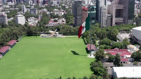 風になびく愛国的なメキシコの国旗を持つ空の荒涼とした人けのない閉鎖されたカンポ・マルテ上空の飛行、メキシコシティ、新型コロナウイルスのパンデミック、ロックダウンと検疫、頭上航空の軌道ショット