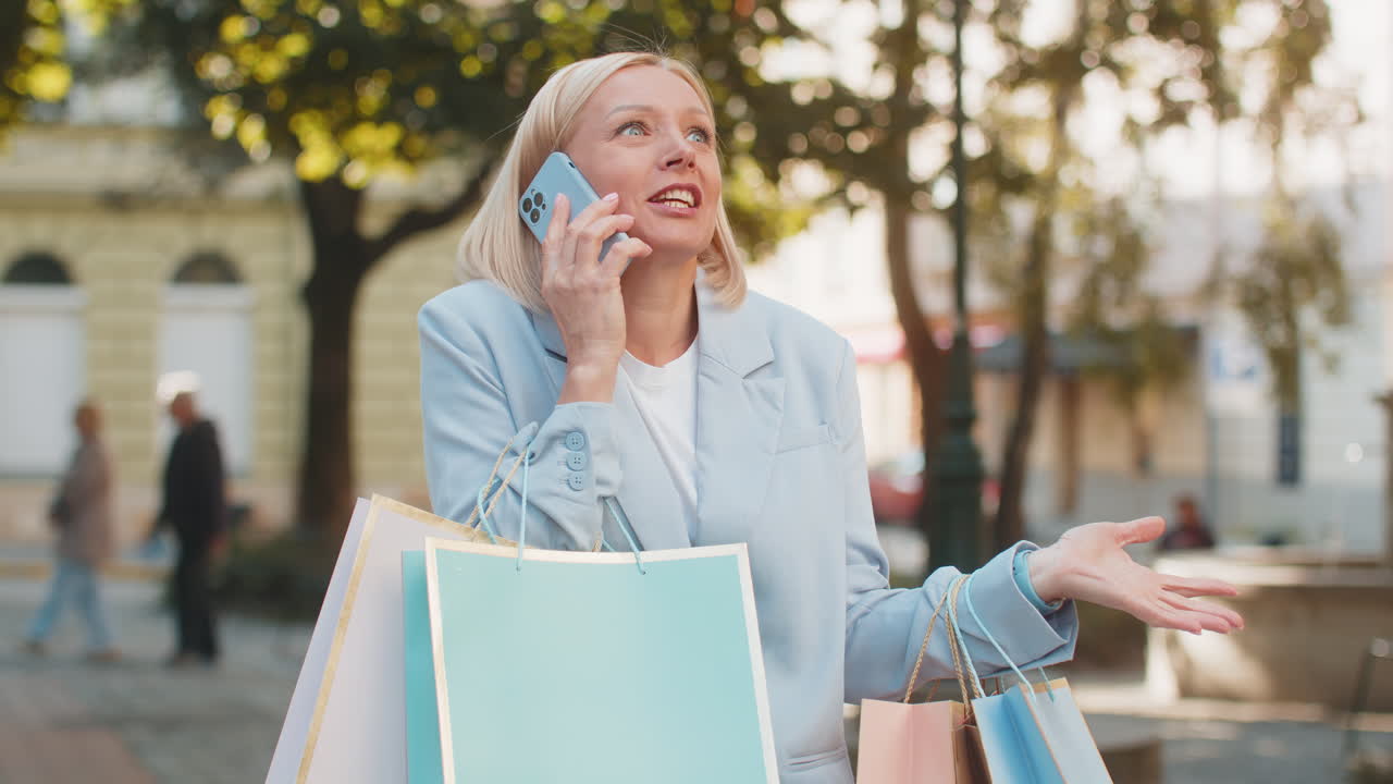 Happy mature businesswoman lady smiling laughs standing on city street holding shopping packages