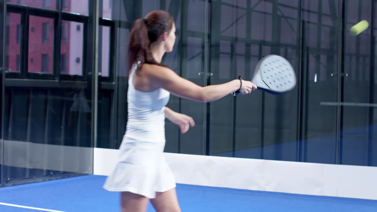 Woman playing padel tennis on indoor court, focusing on hitting ball