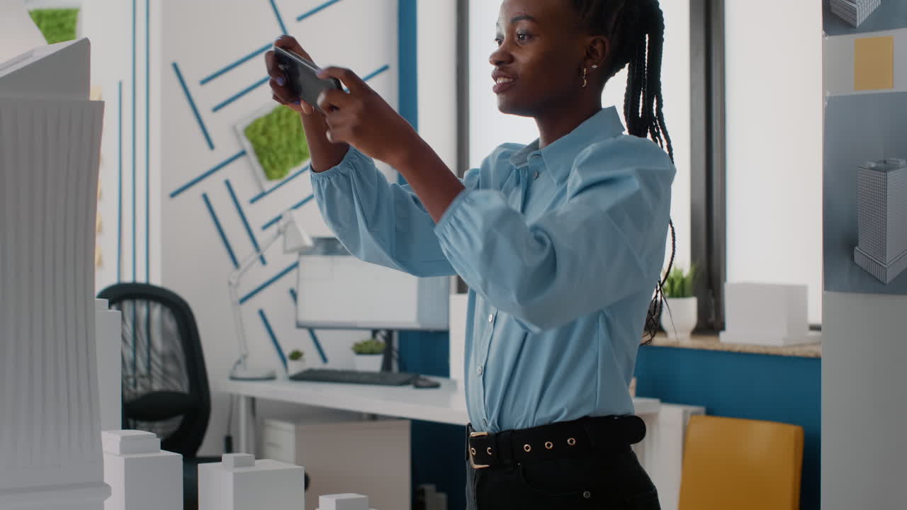 Professional architect taking pictures of a building model with her mobile phone in an office