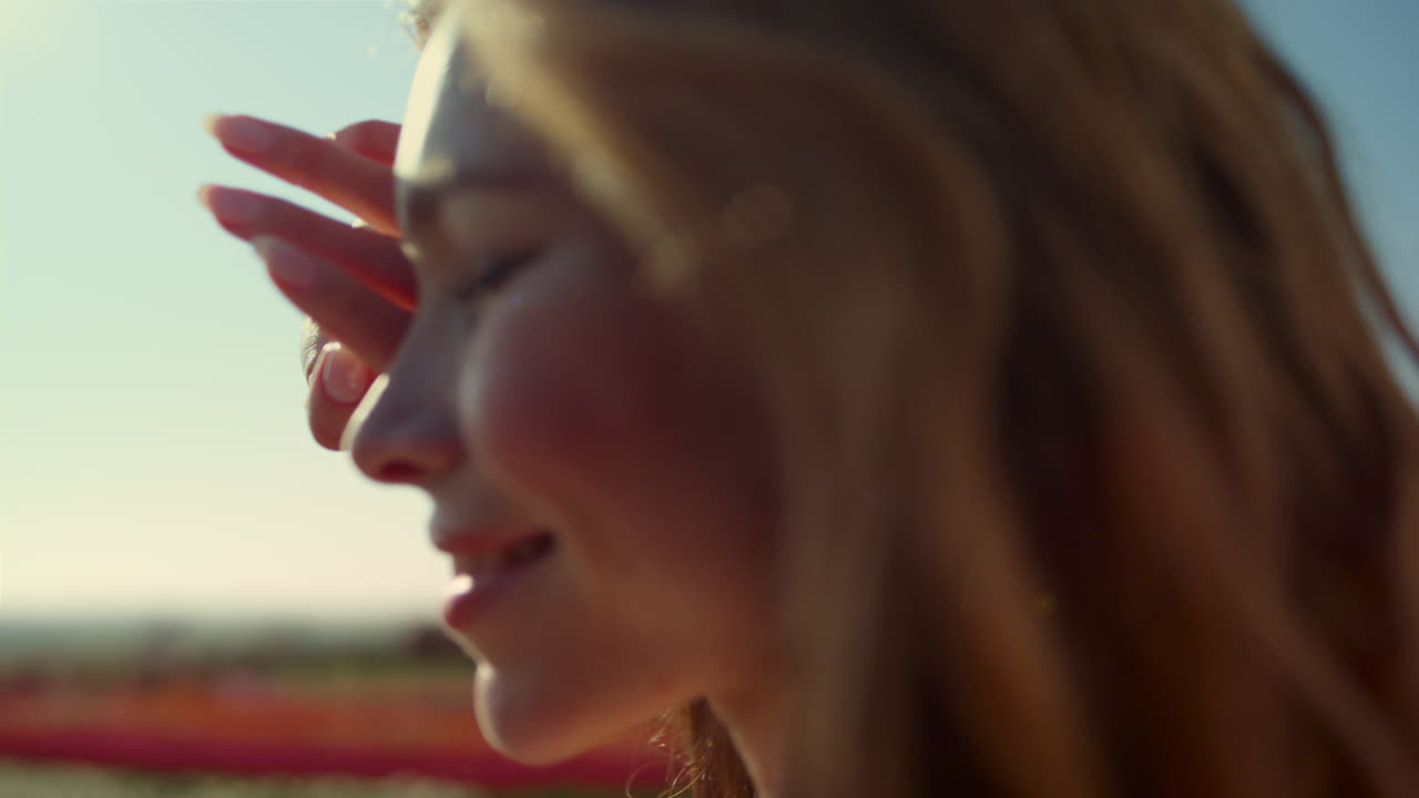 mujer bonita en primer plano mirando la luz del sol brillante en el parque con flores coloridas.