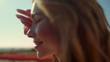 closeup pretty woman looking at bright sunlight in park with colorful flowers.