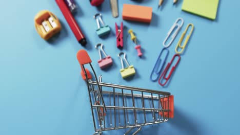 overhead view of shopping trolley and school items on blue background