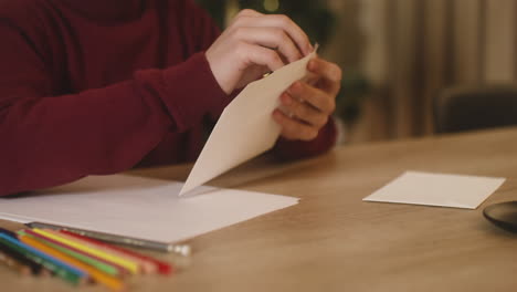 close up view of a child's hands folding a letter of wishes and inserting it in a evelope sitting at a table