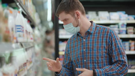 a young man in a supermarket in a protective mask chooses milk and chilled foods