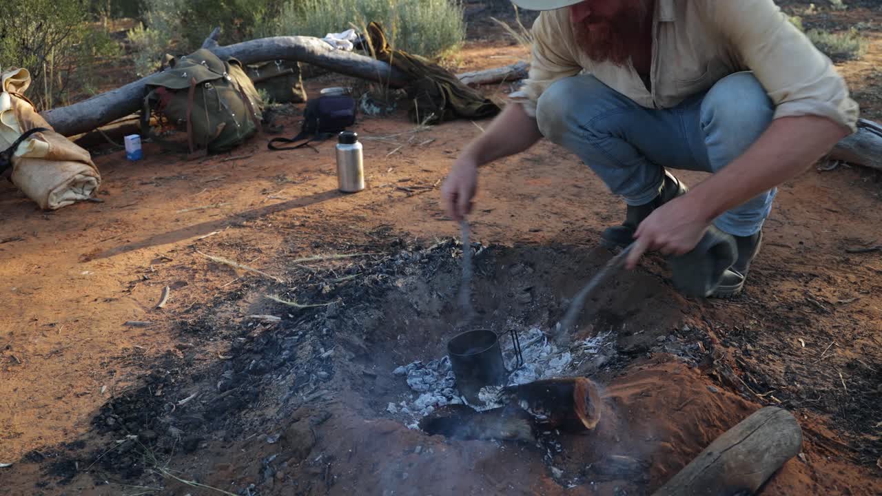 Un boscimano che cucina in un billy di latta su un fuoco da campo nell'entroterra australiano.