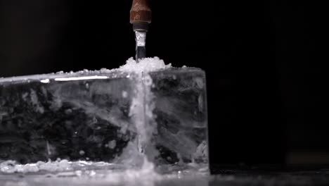 a bartender is splitting the huge clear ice block to two parts by using an ice pick and hammer.