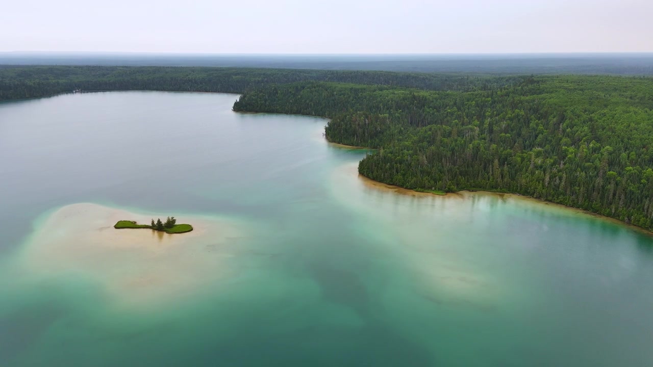 Luftfoto af en græsklædt sandø omgivet af stille turkisblåt vand ved Big Skunk Lake i det nordlige Ontario, med tæt nåleskov der strækker sig til horisonten