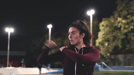 sportive curly girl stretching and rotating arms in the park at night