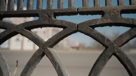 close view of a weathered metal fence with intricate patterns, highlighting the texture and wear of the metal, with cars passing by