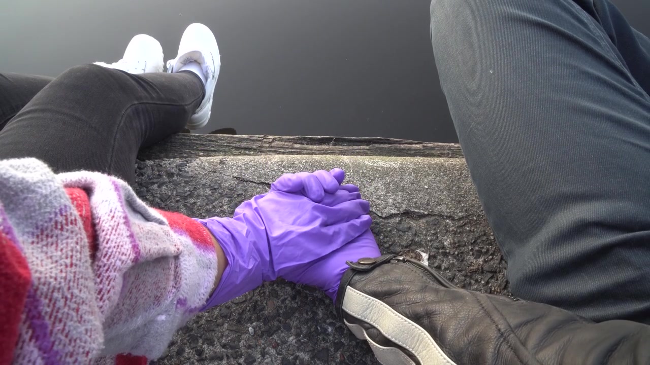 Nahaufnahme eines Paares, das mit Handschuhen Händchen hält, sitzend an einem öffentlichen Ort. Coronavirus-Pandemie-Konzept