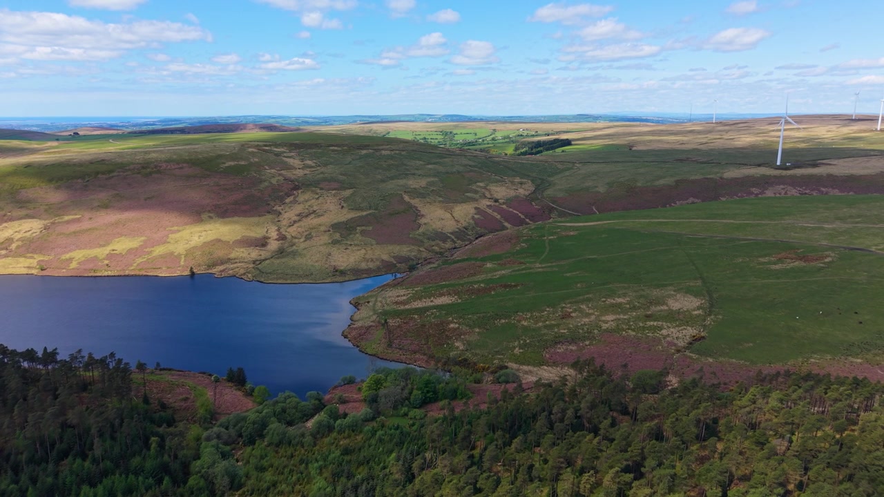 Luftoptagelse der bevæger sig mod Lliw Reservoir med nærliggende vindmøller og skyer, der kaster dramatiske skygger over landskabet. 4K.
