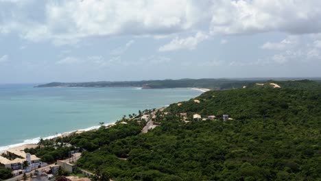 Right-trucking-aerial-drone-extreme-wide-shot-of-the-tropical-Northeastern-Brazil-coastline-with-the-tourist-town-of-Pipa-in-the-background-and-beaches-surrounded-by-cliffs-in-Rio-Grande-do-Norte