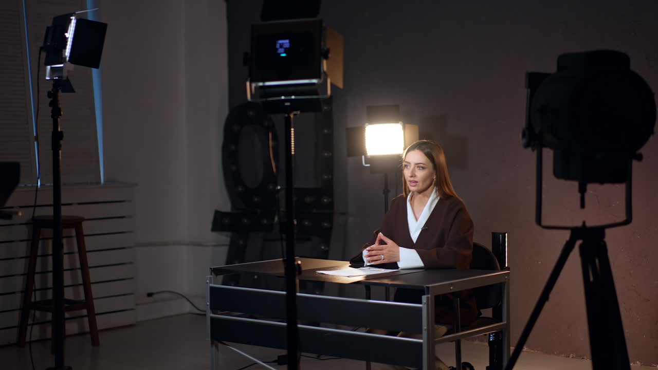 Emotional Caucasian woman talks confidently to camera in modern photo studio. Soffits stand around the reporter.