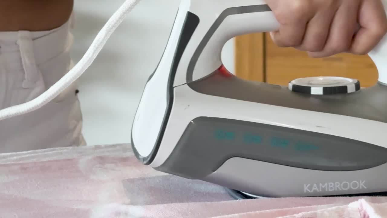 A close-up view of a woman's hand pressing a pink garment with a steam iron