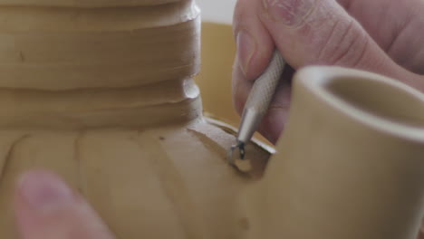 handheld close up shot of adding additional details to an unfinished clay vase right before burning