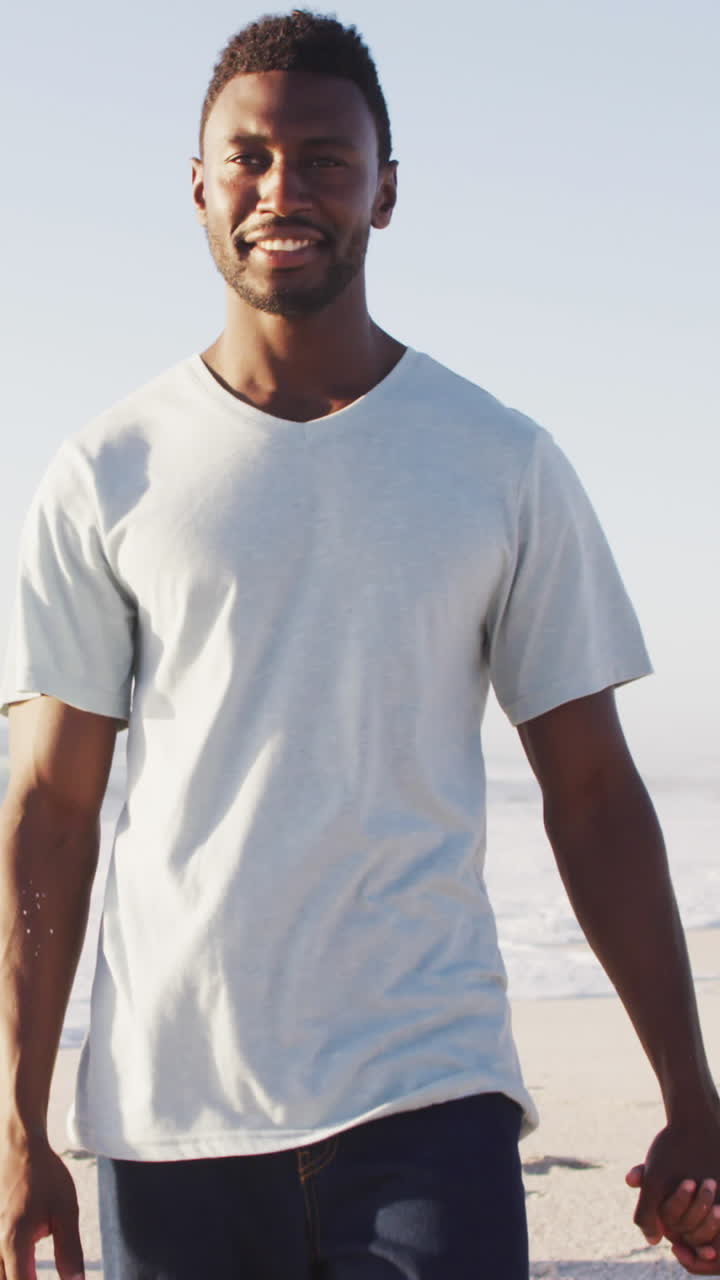 sonriendo afroamericano cogido de las manos y caminando por una playa soleada