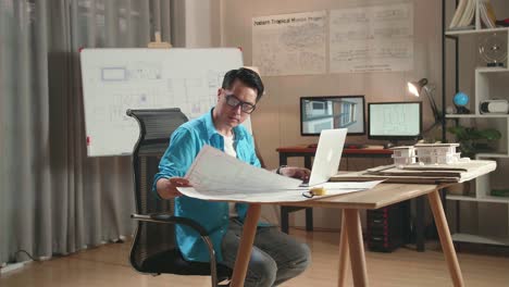 asian man engineer looking at blueprint and typing on a laptop at the office