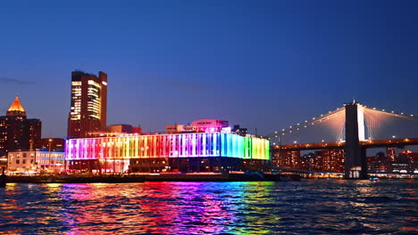 rainbow illumination of pier 17 bar at night. the brooklyn bridge with street lights on at backdrop