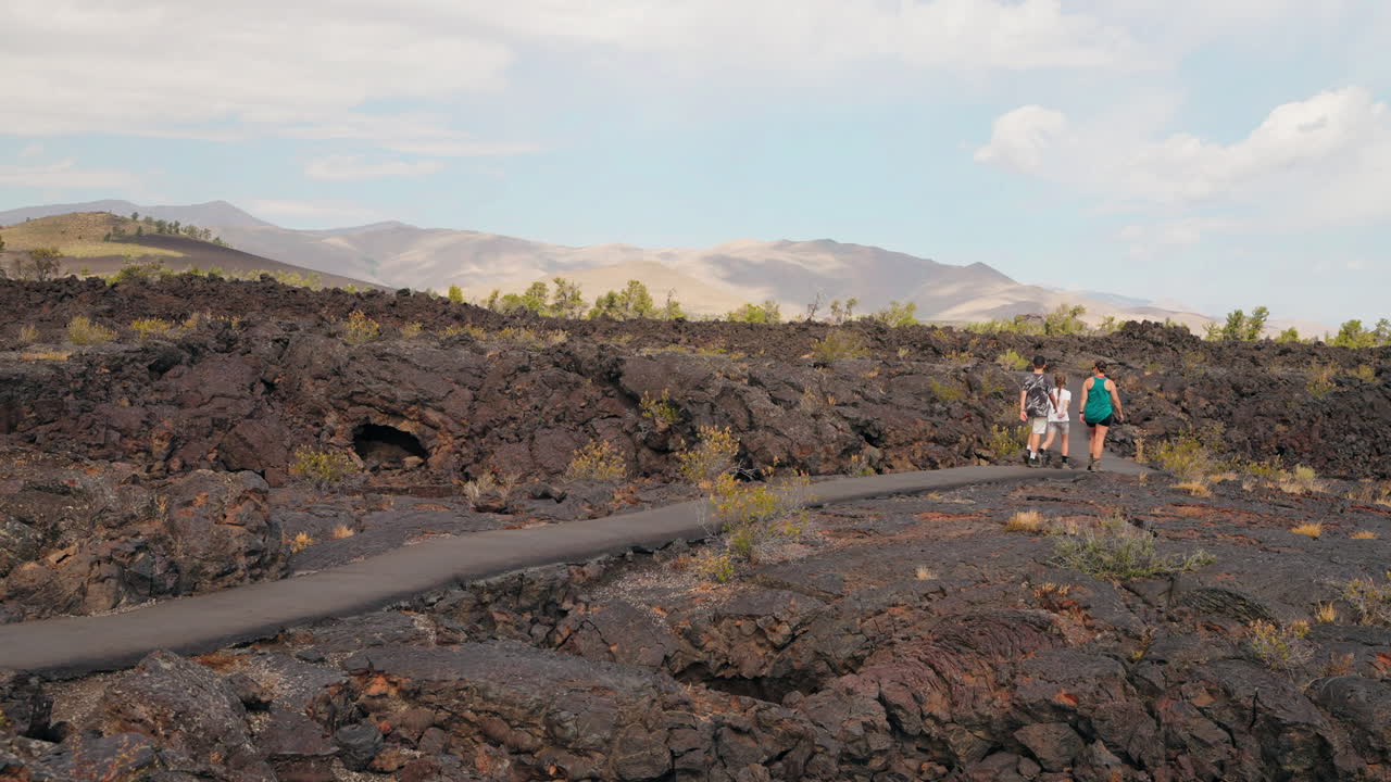 People walk on a paved path through a vast volcanic lava field