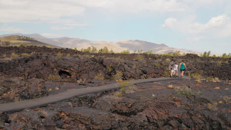 people walk on a paved path through a vast volcanic lava field